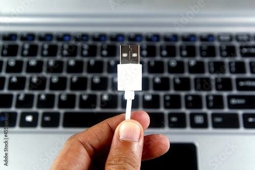 Person holding white USB cable in front of laptop keyboard