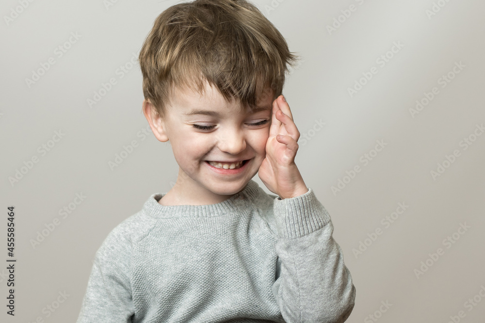 a child of European appearance on a gray background holds a hand near his head. headache in children. emotions a child of European appearance on a gray background holds a hand near his head. headache in children. emotions