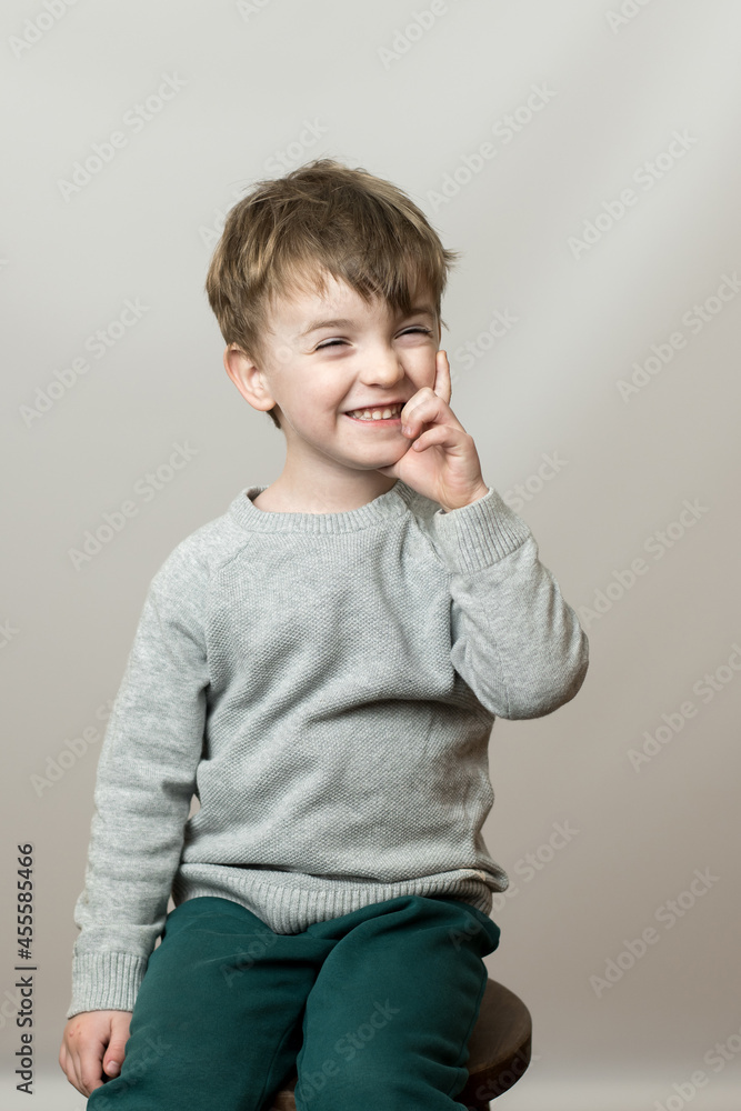 a child of European appearance on a gray background with a smile raises his finger up a child of European appearance on a gray background with a smile raises his finger up