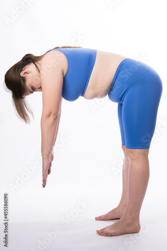 a girl of European appearance in a blue suit is engaged in fitness or yoga. White background. not a perfect figure. Sports training. bends with a straight back