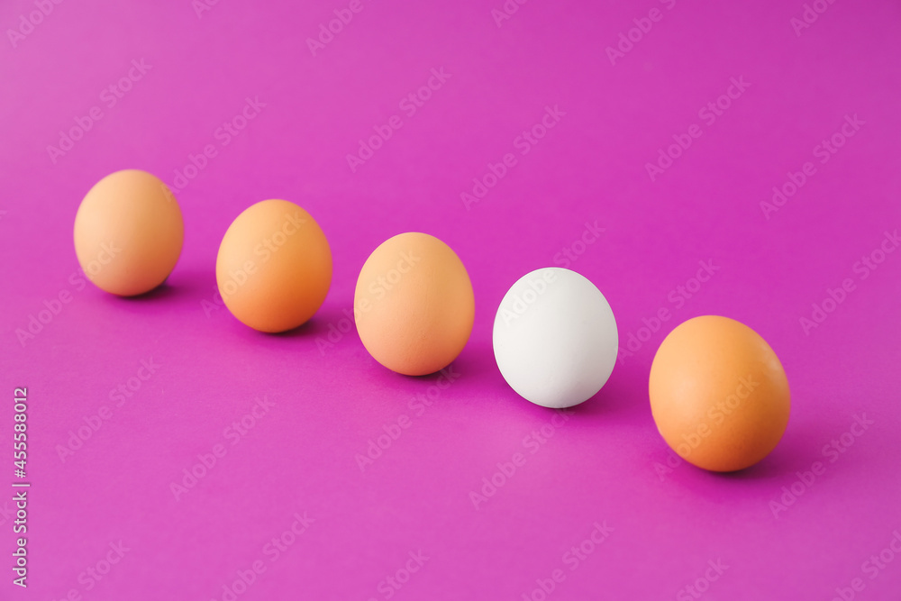 White egg among brown ones on color background. Concept of uniqueness White egg among brown ones on color background. Concept of uniqueness