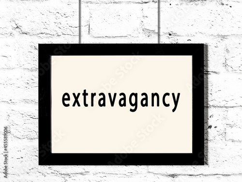 Black frame hanging on white brick wall with inscription extravagancy photo