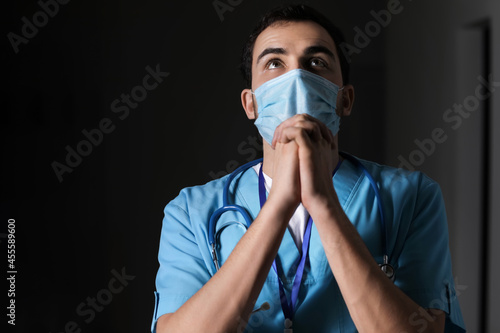 Praying male doctor on dark...