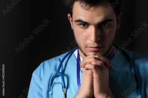 Praying male doctor on dark...
