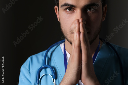 Praying male doctor on dark...