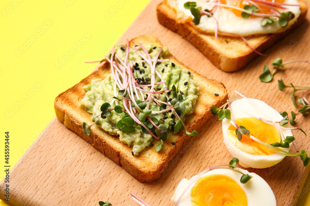 Wooden board with tasty toasts and micro green on color background, closeup