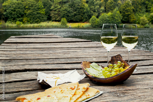 Picnic at the wooden pier by the lake with food, fruit and white wine. Picnic for two, romantic outdoor recreation