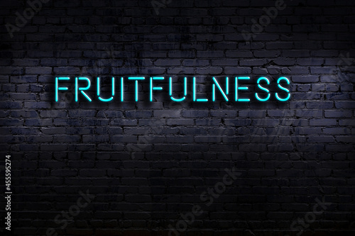 Neon sign. Word fruitfulness against brick wall. Night view