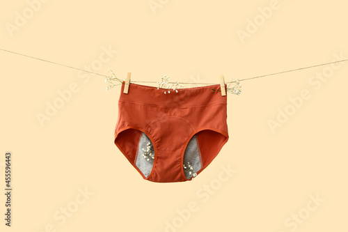 Period panties hanging on rope against color background