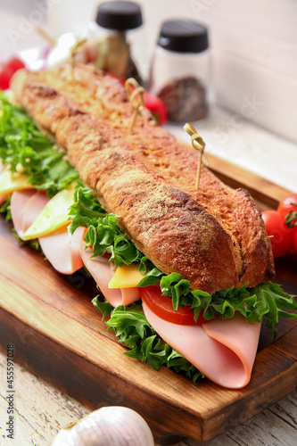 Board with tasty ciabatta sandwich on light wooden background, closeup