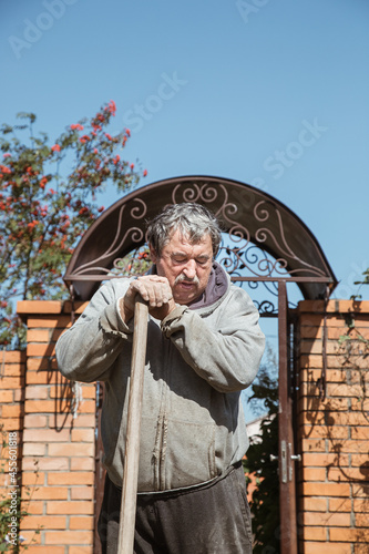 An elderly man leaned on the handle of a shovel for a short rest between work