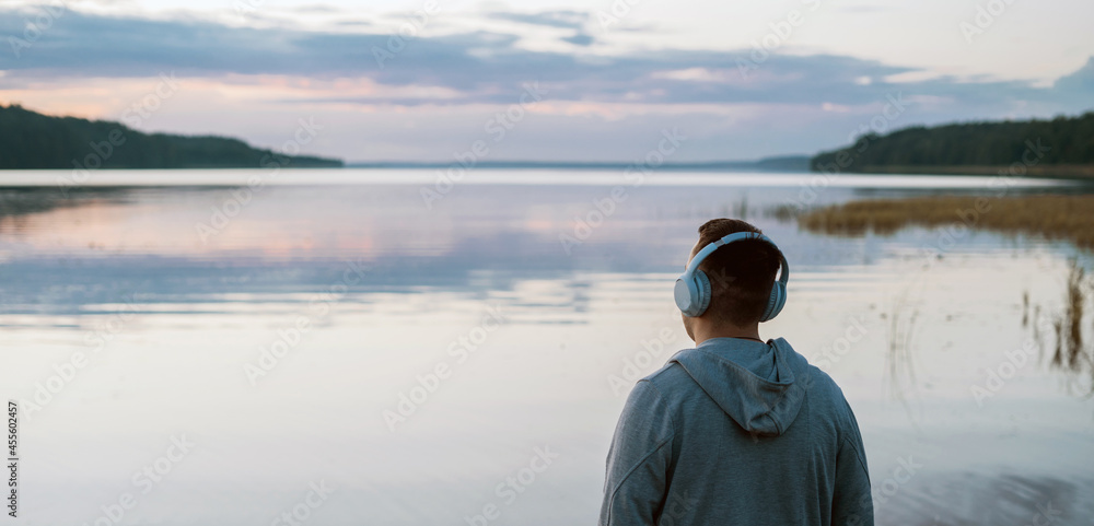 Balance calmness and harmony with yourself. A man meditates with headphones in nature. He listens to pleasant, calm music. - obrazy, fototapety, plakaty 