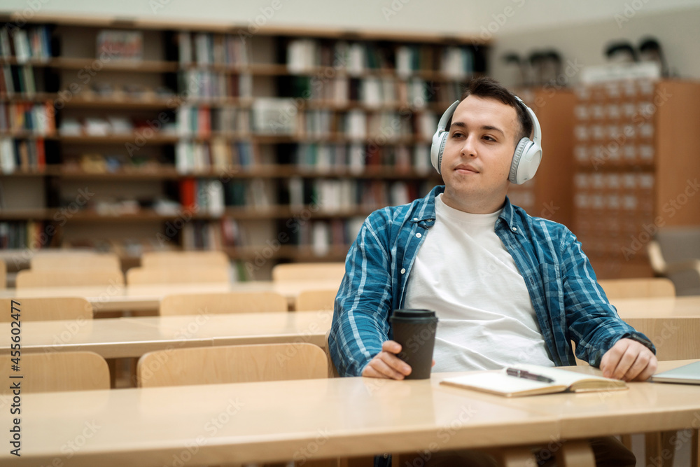 The man is enthusiastically studying at the institute. He listens to an e-book in the university library with wireless headphones. The man is enthusiastically studying at the institute. He listens to an e-book in the university library with wireless headphones.