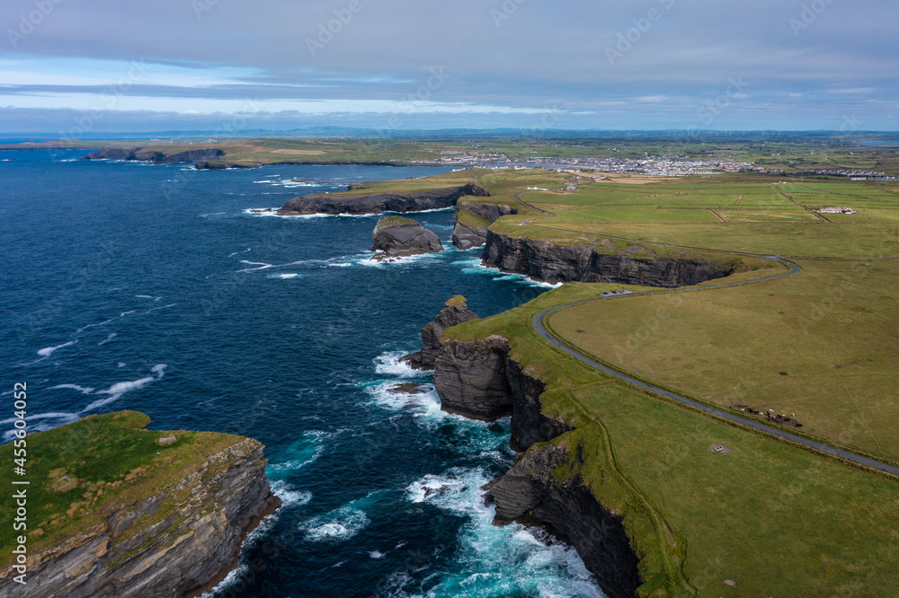 Aerial view of beautiful and green mountain of the famous tourist landmark Moher Cliff in Ireland with sea waves hitting rocks during day under cloudy sky Aerial view of beautiful and green mountain of the famous tourist landmark Moher Cliff in Ireland with sea waves hitting rocks during day under cloudy sky