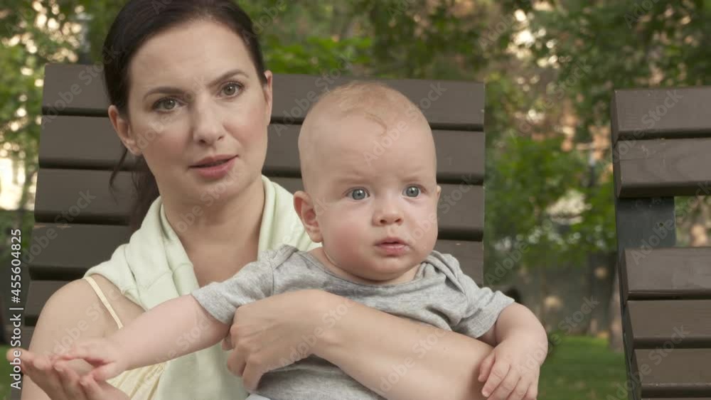 Mother with baby on sun lounger in public park on a sunny summer day, adult mother is keeping on her arms and playing with six month old baby boy. High quality 4k footage Mother with baby on sun lounger in public park on a sunny summer day, adult mother is keeping on her arms and playing with six month old baby boy. High quality 4k footage