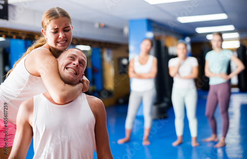 Young woman performing chokehold movement on man during group self-defence training.