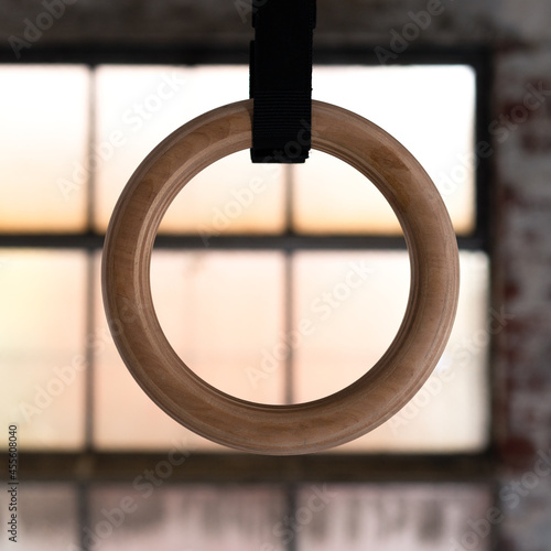 Traditional wooden gymnast rings hanging from black straps in dramatic sunset sky outside the window