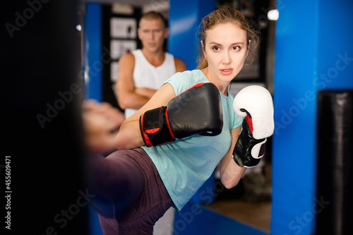 Young european boxer woman in boxing gloves is practicing different kicks at gym