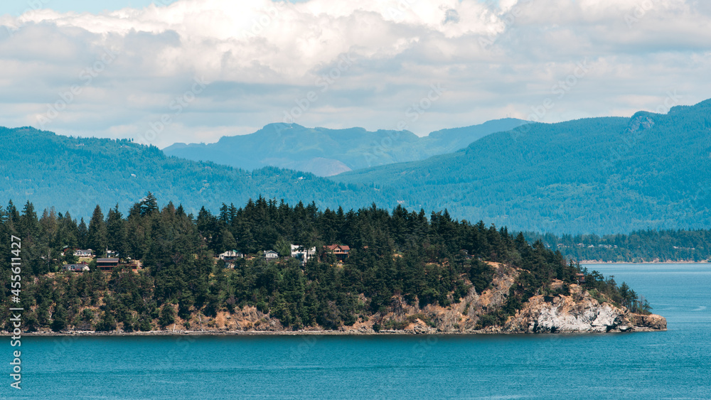 Forested island in the bay with mountains in the background.