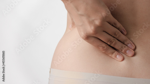 Backache. Female hand touches and presses on lower back on white background. Close-up
