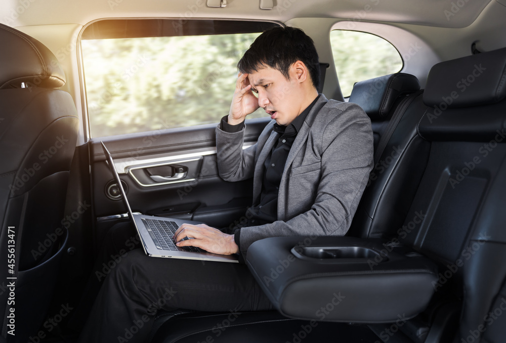 stressed business man using laptop computer while sitting in the back seat of car