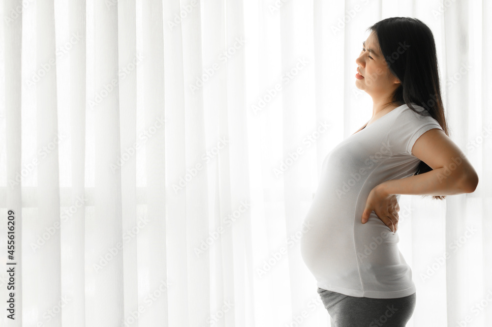 Asian pregnant woman standing with hand on back feeling pain from backache