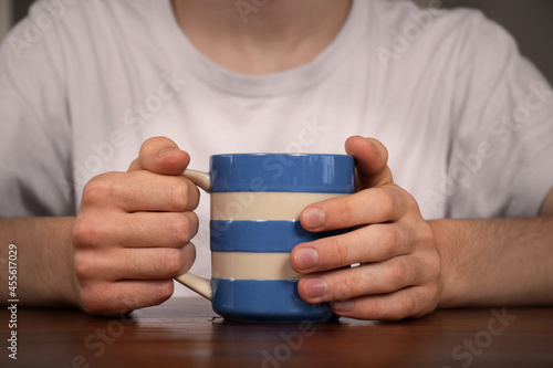 Foto A young man sits at a table holding a hot drink in a mug