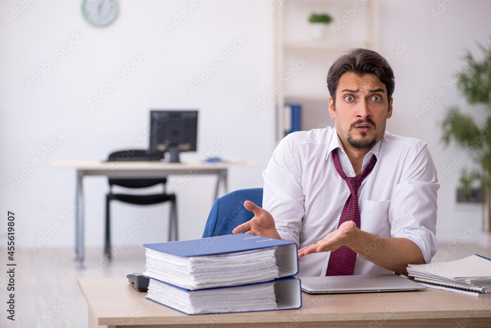 Young male employee unhappy with excessive work in the office Young male employee unhappy with excessive work in the office