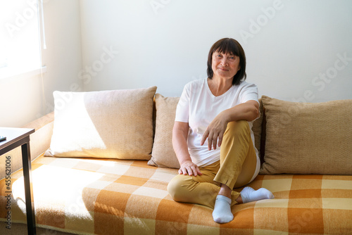 Portrait shot in head of peaceful calm middle aged woman relaxing on cozy sofa alone at home. Nice happy 60s old mature grandmother relaxing on living room couch posing for photo.