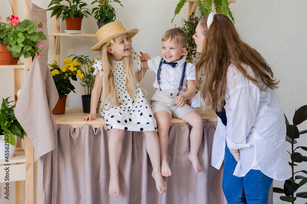 a young mother with her son and daughter laughs, hugs and plays indoors with home flowers. a girl and a boy are sitting. Concept of a happy, fun family. Lifestyle, space for text. High quality photo