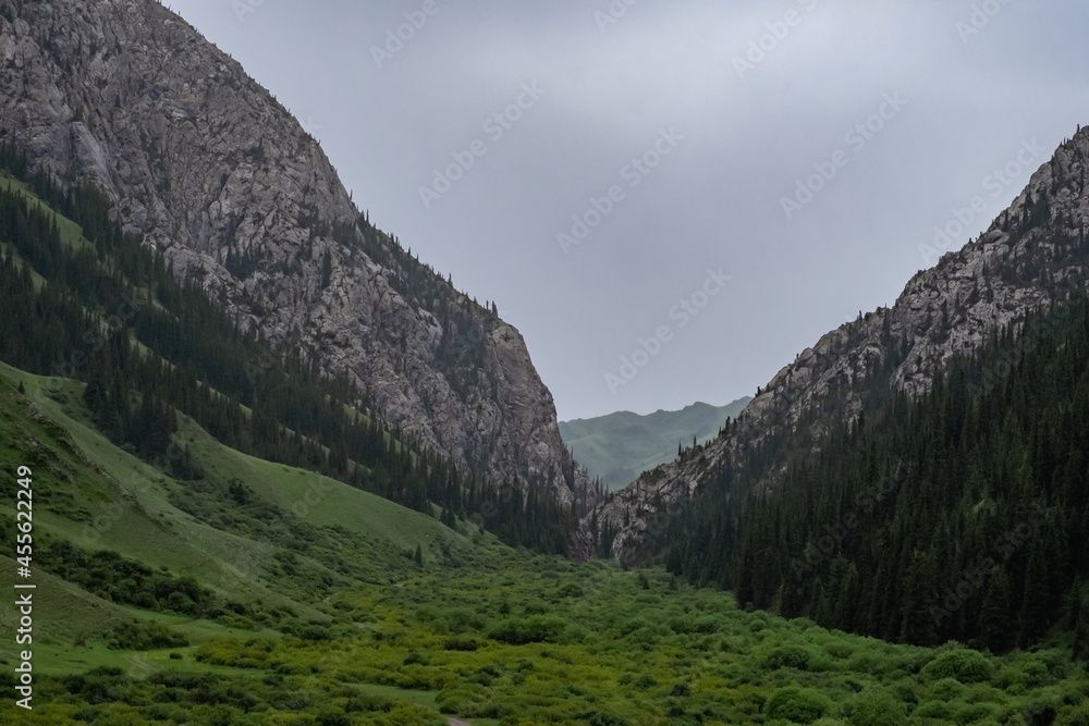 Beautiful rocky mountains with green forest on foothills with rainy clouds. Beautiful summer landscape. Komirshi gorge in Kazakhstan. Travel tourism concept. Beautiful rocky mountains with green forest on foothills with rainy clouds. Beautiful summer landscape. Komirshi gorge in Kazakhstan. Travel tourism concept.