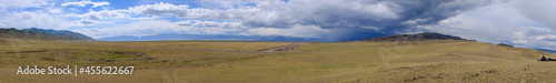 Panoramic view to steppe with mountains and cloudy sku on background.