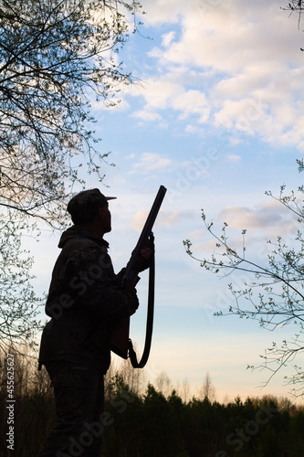 a hunter with a shotgun at the ready stands in the evening twilight