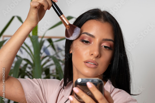 Beautiful long black-haired young woman puts makeup on her face in beauty studio