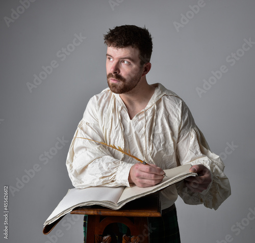 Wallpaper Mural Close up portrait of handsome brunette man wearing Scottish kilt and renaissance white  pirate blouse shirt. Holding a quill and writing in a book,  pose isolated against studio background.    Torontodigital.ca