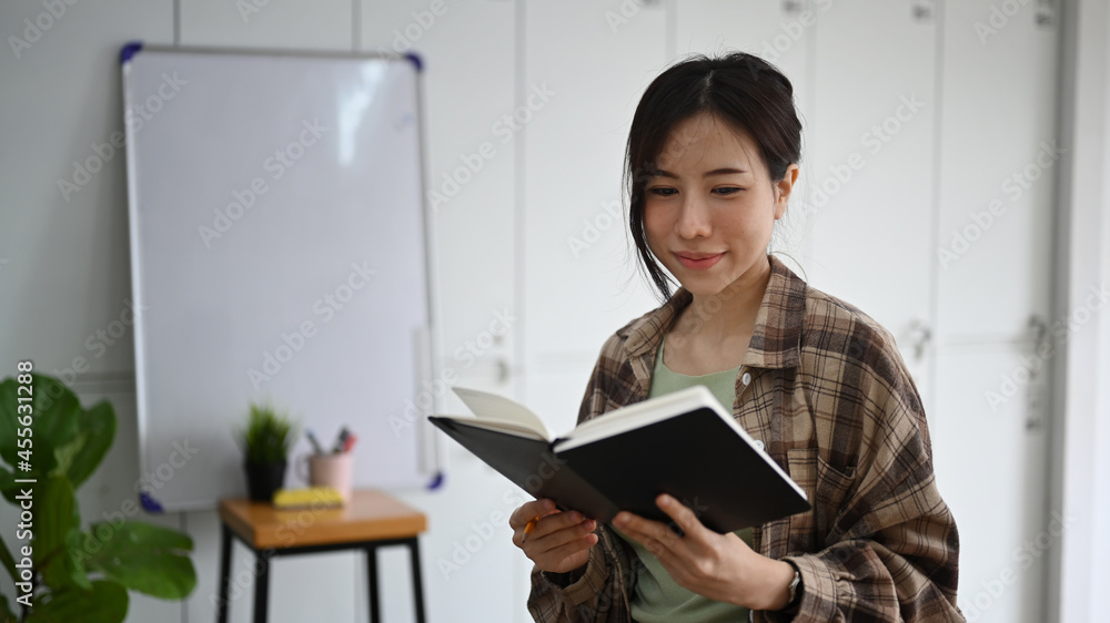 Thoughtful young woman reading a book while sitting in modern workplace. Thoughtful young woman reading a book while sitting in modern workplace.