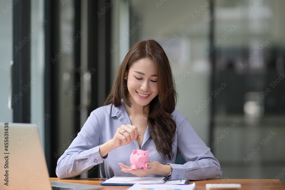 Smiling young Asian woman putting coin into piggy bank. Business investment finance accounting concept. Smiling young Asian woman putting coin into piggy bank. Business investment finance accounting concept.