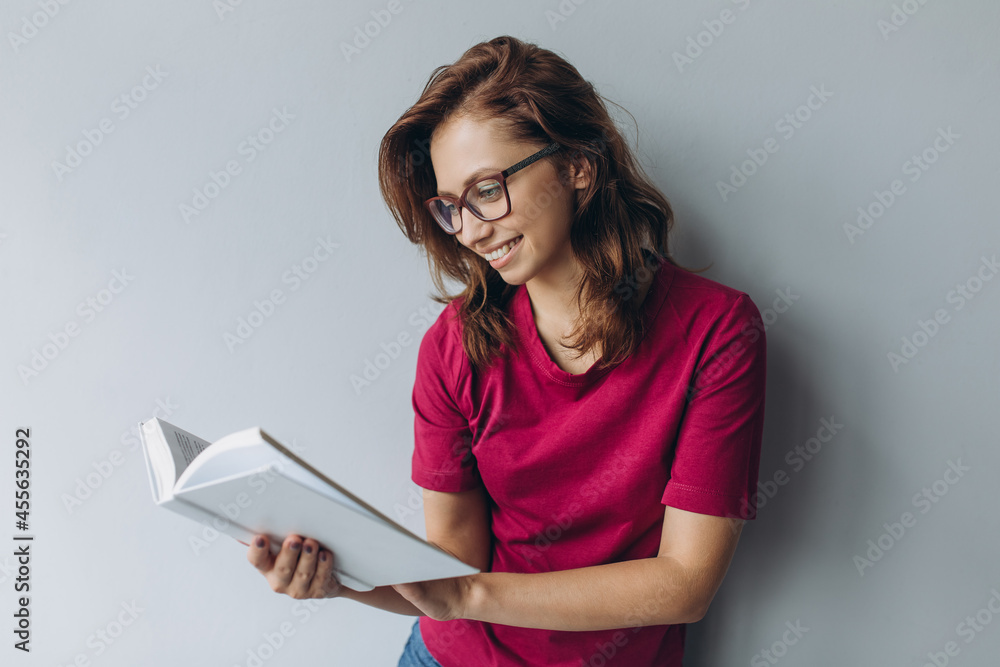 Portrait of beautiful young brunette woman in eye glasses holding book isolated on grey background Portrait of beautiful young brunette woman in eye glasses holding book isolated on grey background