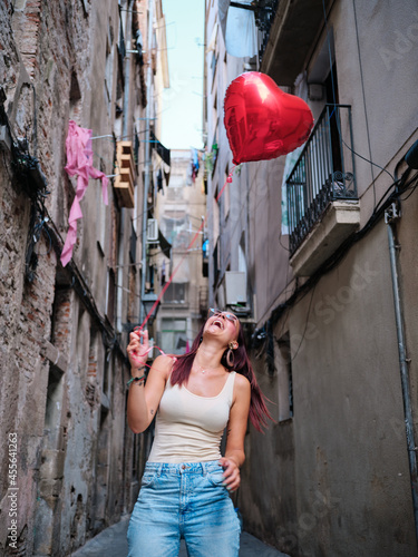 Cheerful woman holding a red heart balloon outdoors.