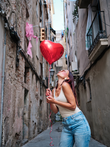 Woman with a red heart-shaped balloon outdoors on the street.
