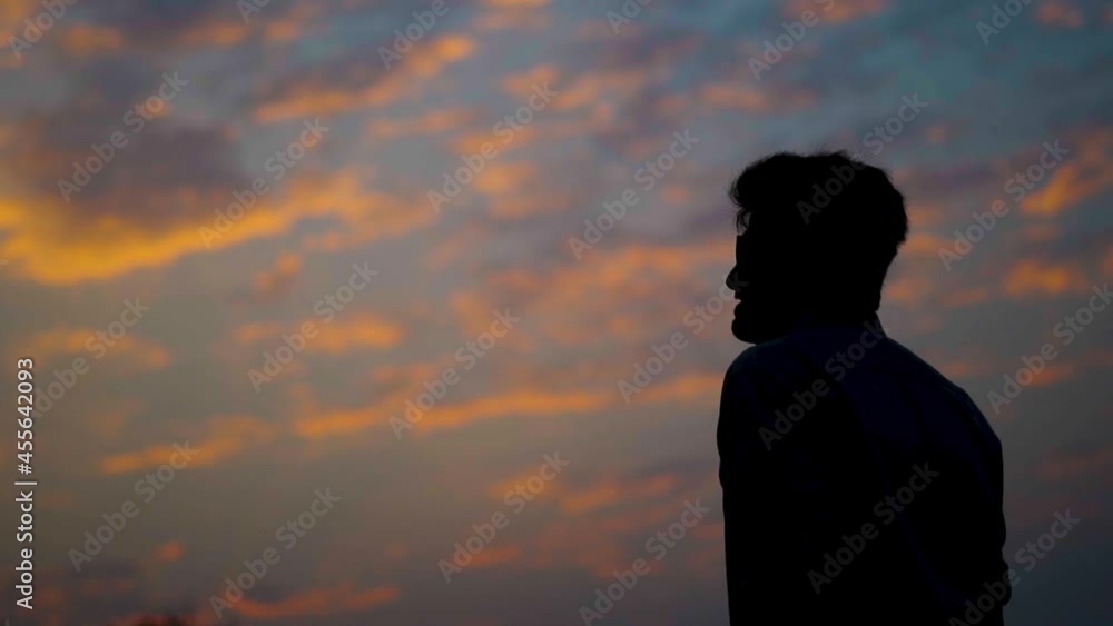 Silhouette of an Indian man staring at the sky with orange clouds during the sunset. Man looks at the sky searching for hope. Hope concept. Inspiration background with copy space. Silhouette of an Indian man staring at the sky with orange clouds during the sunset. Man looks at the sky searching for hope. Hope concept. Inspiration background with copy space.