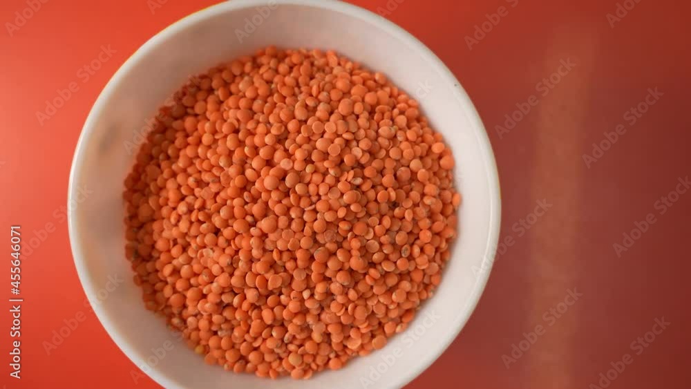 Some lentil grains on a clay bowl on top of red background