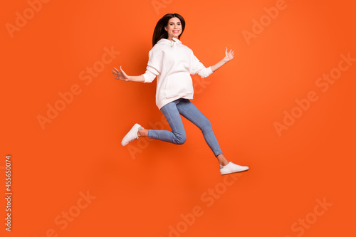Full length body size view of attractive lucky cheerful girl jumping running isolated over bright orange color background