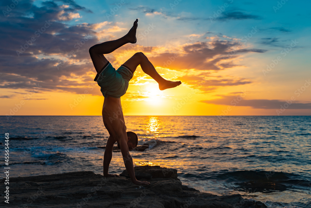 A fit young man practices yoga poses on the beach during sunset