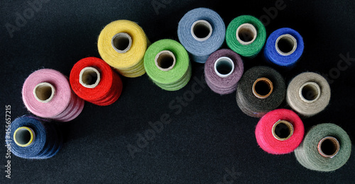 many colorful spools of thread top view on black background
