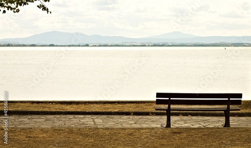 An empty wooden bench in a park facing Lake Trasimeno (Umbria, Italy, Europe)