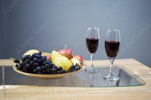 glasses with red wine on the table and a bowl with fruit grapes apple and pear