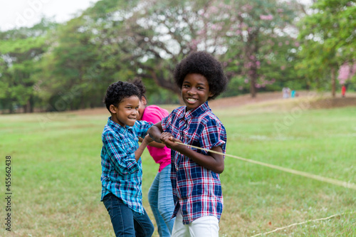 Group of African American boy and girl playing tug of war together in the park. Cheerful children with curly hair having fun with tug of war. Black children people playing tug of war