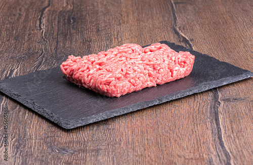Fresh minced meat on a stone slate board over a wooden background.