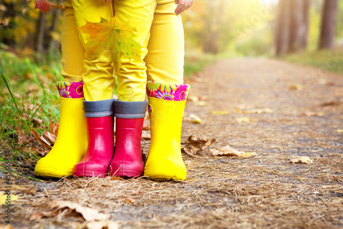 Feet in red and yellow rubber boots of a mother and daughter in the autumn forest. Seasonality, seasons, fallen dry maple leaves, family walk, feeling of love and care, parenthood photo